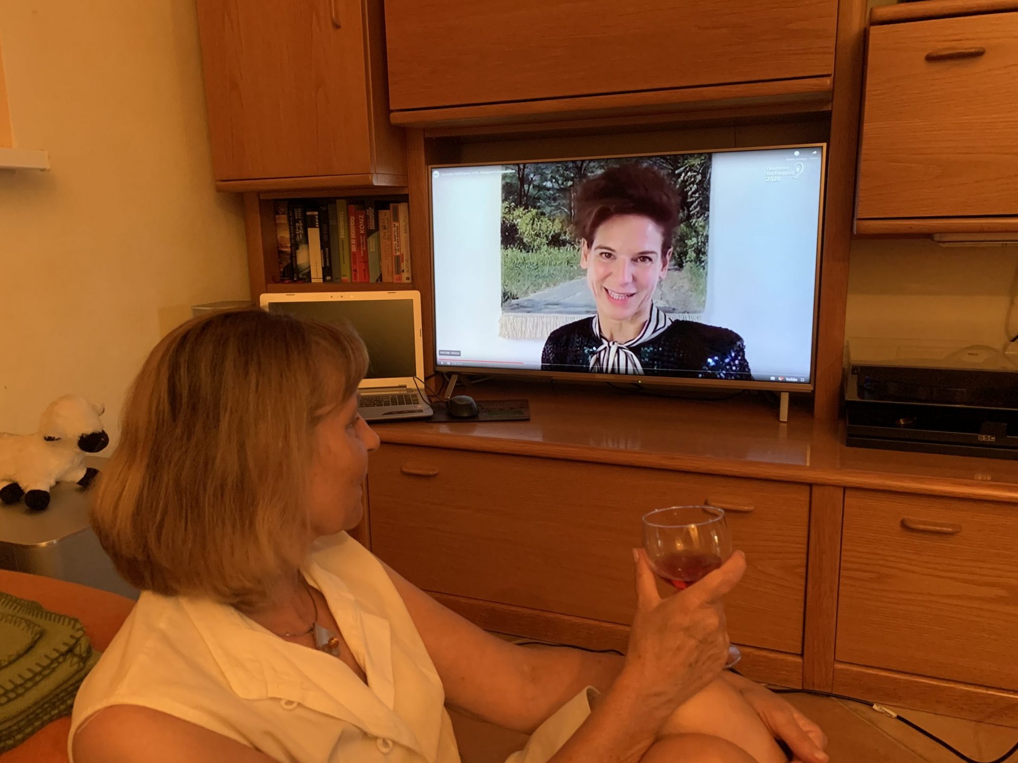 Die Blindgängerin sitzt vor einem TV-Bildschirm, auf dem Bibiana Beglau zu sehen ist. Mit einem Weinglas prostet sie der Schauspielerin zu.