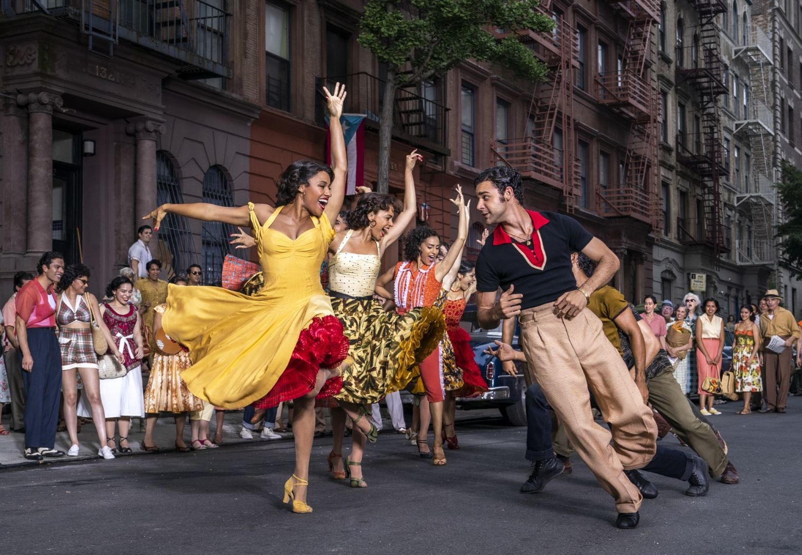 In einer Straße von New York tanzen ausgelassen junge Frauen und Männer in bunten Kostümen.