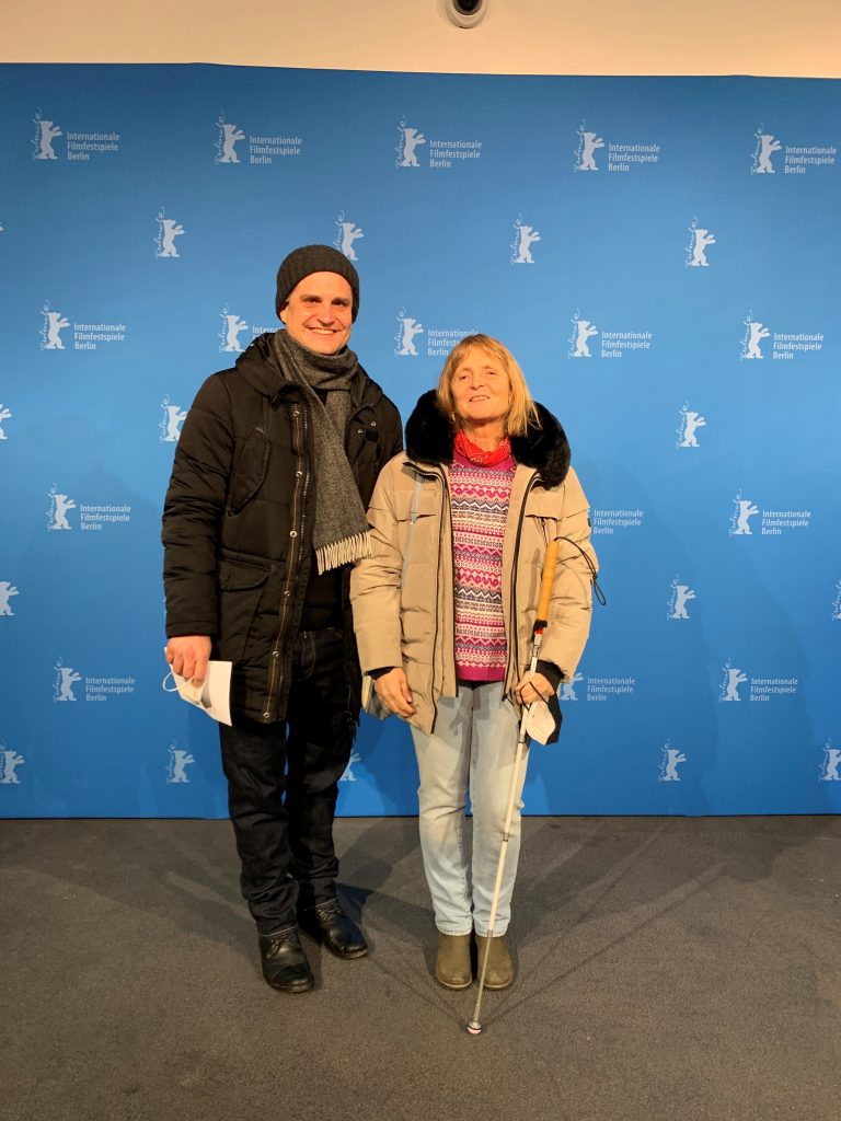 Andres Schüpbach vom Team "Greta und Starks" mit der Blindgängerin vor einer hellblauen Wand mit den Logos der Berlinale: Die weiße Silhouette eines Bären, daneben der Schriftzug "Internationale Filmfestspiele Berlin".